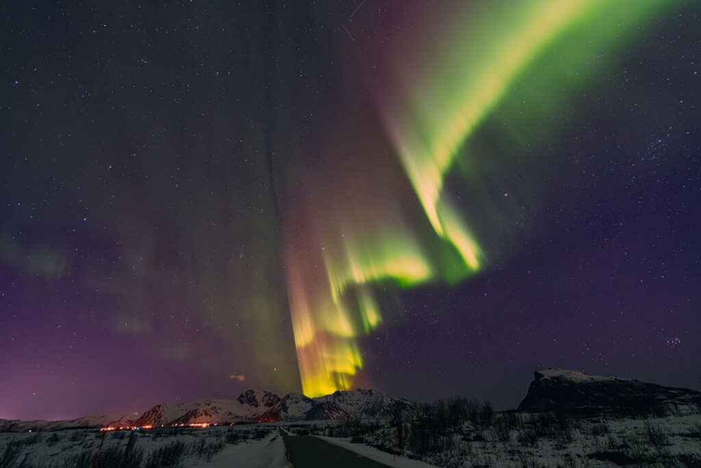 Intensive grüne und violette Nordlichter (Aurora Borealis) über einer verschneiten Gebirgslandschaft auf den Lofoten, fotografiert während einer Fotoreise von hemmi.photo.