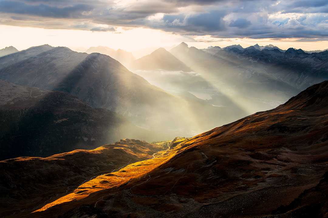 Atemberaubende Aussicht von der Alp Languard in Pontresina auf die Alpen im Oberengadin mit dramatischen Sonnenstrahlen bei Sonnenuntergang.