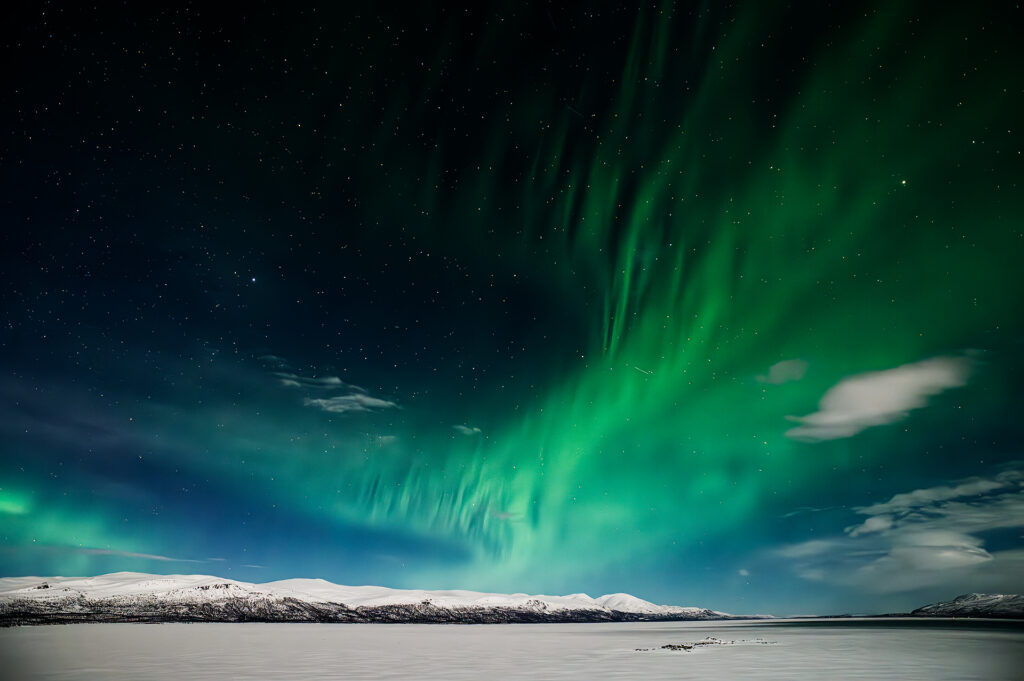 Grüne Polarlichter über schneebedeckten Bergen und zugefrorenem See in Lappland, Finnland