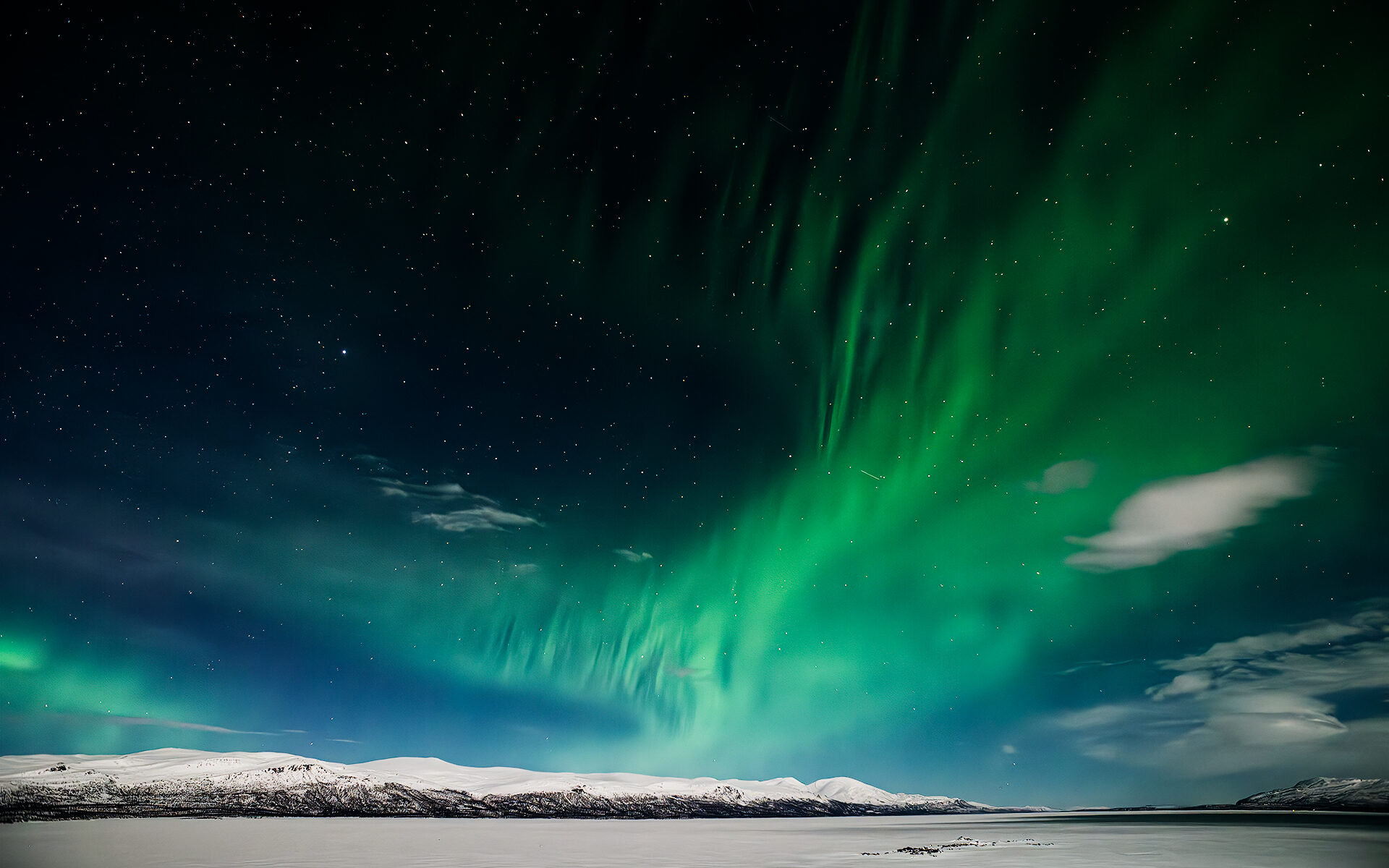 Grüne Polarlichter über schneebedeckten Bergen und zugefrorenem See in Lappland, Finnland
