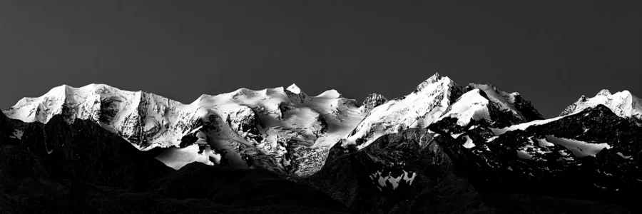 Engadin – Wo Licht auf ewiges Eis trifft. ramatisches Schwarzweiß-Panorama der schneebedeckten Berninagruppe in den Schweizer Alpen – Teaser für die Engadin-Kollektion von Hemmi.photo.