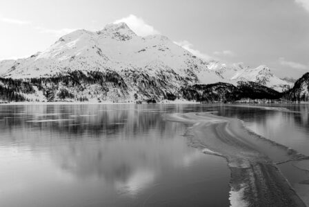 <a href="https://shop.hemmi.photo/products/frozen-wave" target="_blank >Hier klicken zum Shop</a> Ein gefrierender Schweizer Bergsee im Winter in Schwarz-Weiss, auf dessen teils eisbedeckter Oberfläche sich ein grosser verschneiter Berggipfel spiegelt.